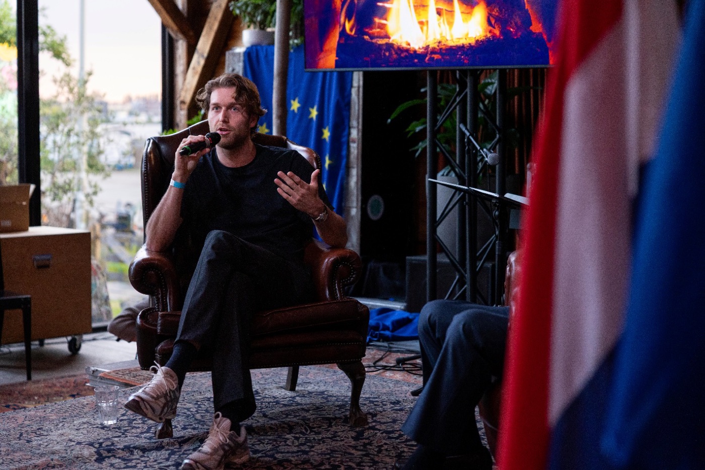Thomas Huttinga spreekt met microfoon tijdens de Nacht van Europa van D66, met de Europese vlag op de achtergrond